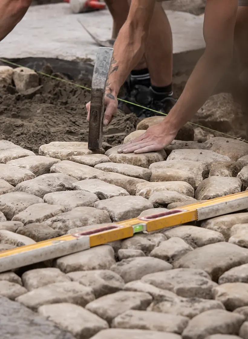 Oude kasseien worden in een zandbed gelegd met hamer, waterpas en richtsnoer