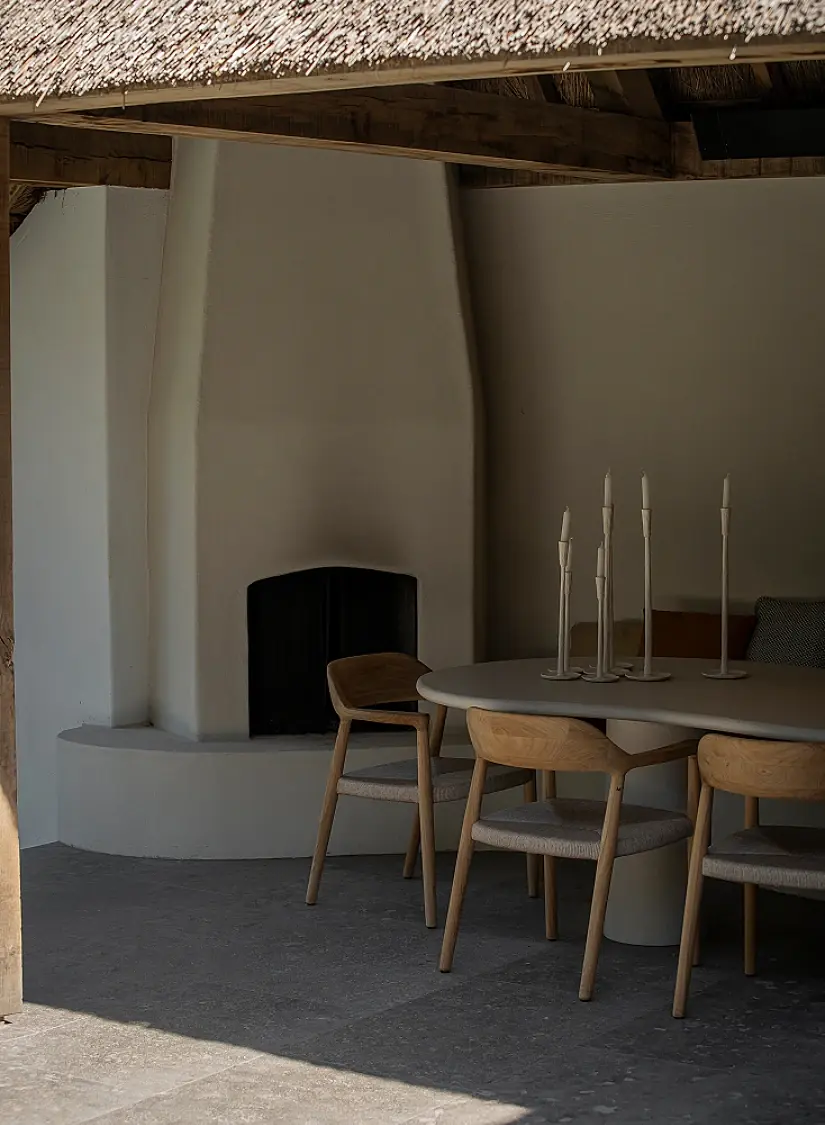 Overdekt terras onder een rieten dak met witte buitenhaard, eettafel en houten stoelen
