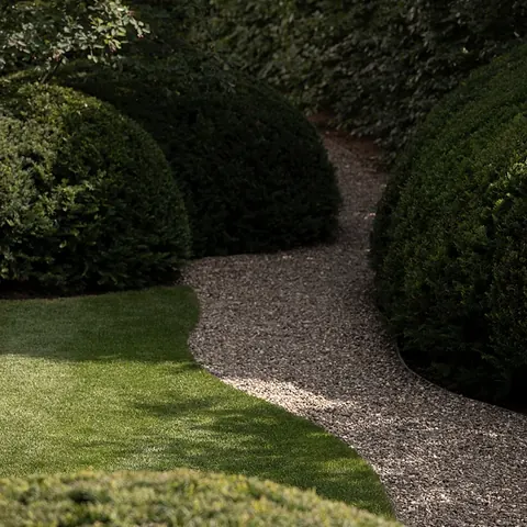 Slingerend grindpad met een metalen boordrand tussen gazon, geschoren bollen en taxus