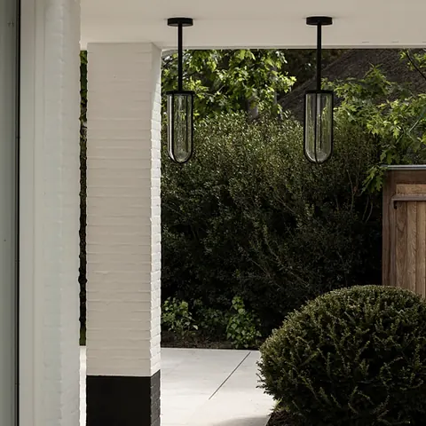Overdekt terras in lichte natuursteen met zwarte hanglampen en een bol in buxus