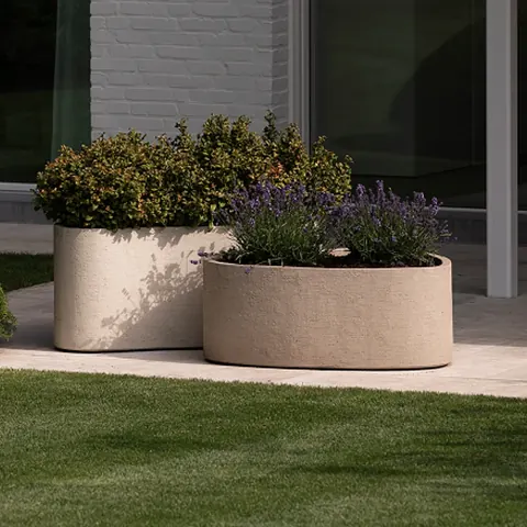 Twee zandkleurige plantenbakken met lavendel en een heester op een terras in lichte tegels