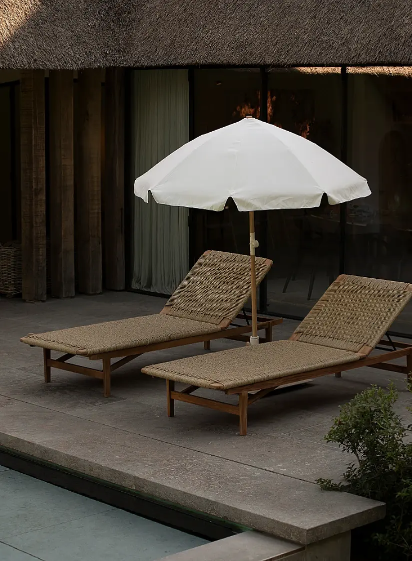 Twee ligbedden en een witte parasol op een terras in grijze natuursteen bij het zwembad